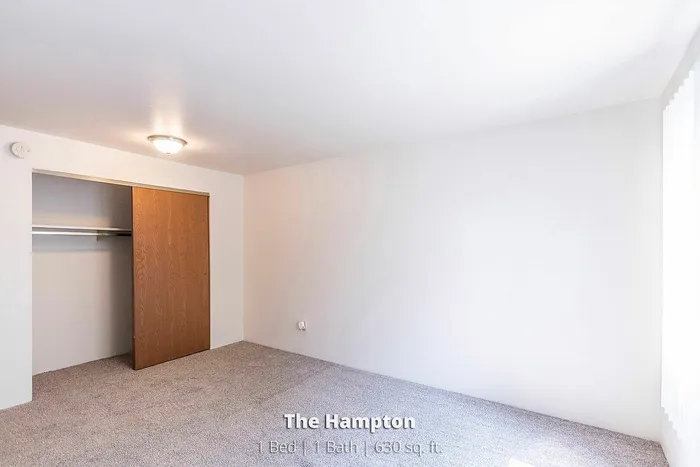 Bright and inviting bedroom in The Hampton apartment featuring a spacious closet and soft carpet flooring, ideal for cozy living.