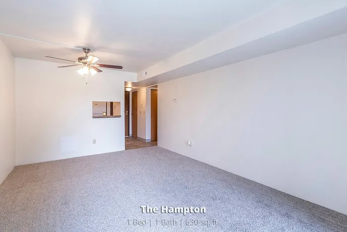 Bright and inviting living space in The Hampton, featuring modern ceiling fan and plush carpeting, perfect for a cozy 1 bed, 1 bath apartment with 630 sq ft of comfort.