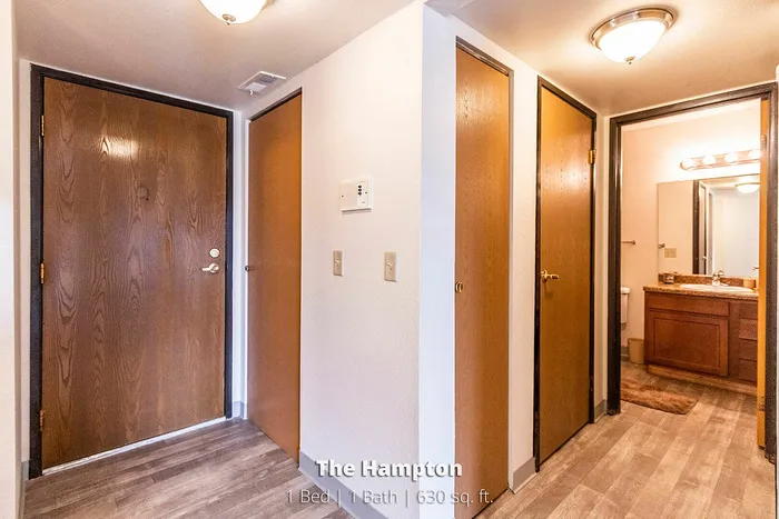Inviting entrance with warm wooden doors leading to a cozy bathroom, showcasing The Hampton's stylish 1 Bed, 1 Bath apartment, 630 sq. ft.