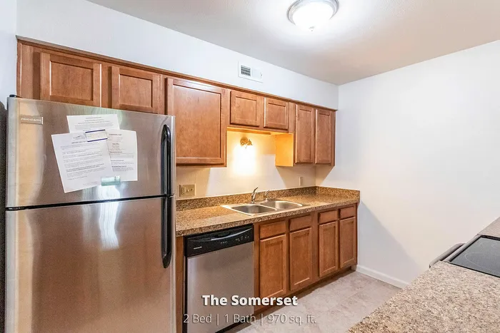 Inviting kitchen in The Somerset apartment featuring sleek stainless steel appliances, warm wooden cabinetry, and elegant granite countertops. 2 Bed, 1 Bath, 970 sq. ft.