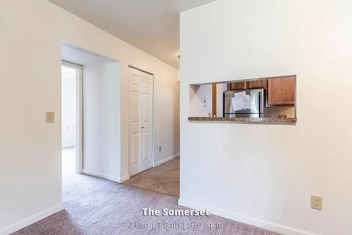 Inviting apartment interior with cozy carpeting leading to a sleek kitchen area, showcasing The Somerset's 2 bed, 1 bath layout in 970 sq. ft.