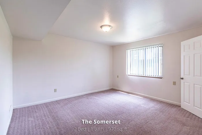 Bright bedroom with soft carpeting and natural light, part of The Somerset's spacious 2 bed, 1 bath, 970 sq ft apartment.