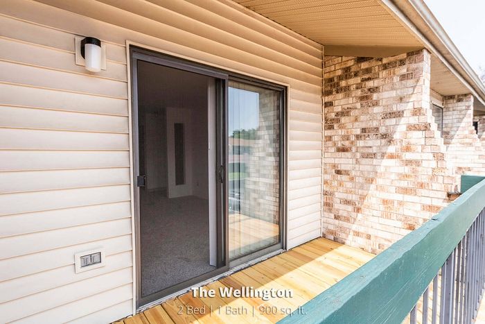 Cozy balcony view from The Wellington featuring sliding glass doors, perfect for a 2 bed, 1 bath apartment with 900 sq. ft. of comfortable space.