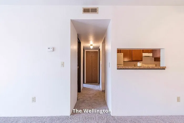 Inviting corridor leading to a cozy and spacious kitchen with warm wood cabinetry, part of The Wellington's 2 Bed 1 Bath apartment spanning 900 sq. ft.
