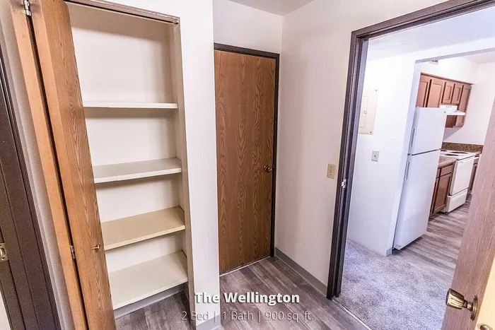Inviting hallway in The Wellington apartment showcasing a built-in closet, warm wood tones, and a glimpse into a modern kitchen. Ideal for comfortable living in 900 sq. ft.