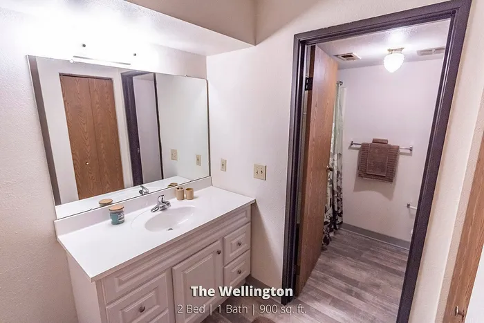 Bright and elegant bathroom in The Wellington apartment, featuring a large mirror, modern fixtures, and ample storage. Ideal space in a cozy 2 bed, 1 bath, 900 sq. ft. home.
