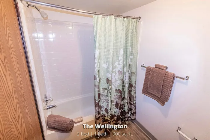 Inviting bathroom with modern fixtures, featuring a chic floral shower curtain and soft brown towels at The Wellington, 2 Bed, 1 Bath, 900 sq. ft.