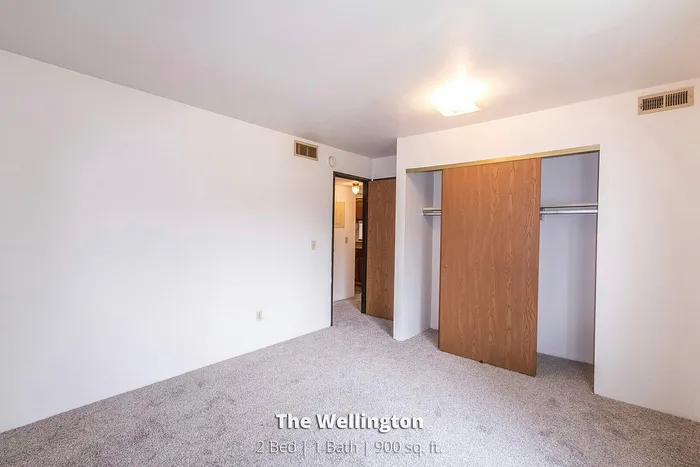 Bright and spacious bedroom in The Wellington with carpet flooring, built-in closets, and modern lighting, perfect for comfort and style.