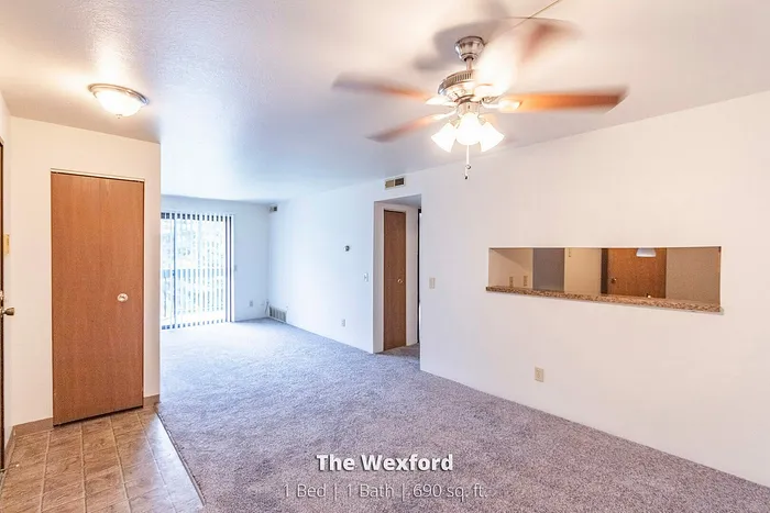 Inviting living space in The Wexford, featuring a cozy carpeted area, elegant ceiling fan, and sliding glass doors, perfect for a comfortable lifestyle in 1 Bed, 1 Bath, 690 sq. ft. apartment.