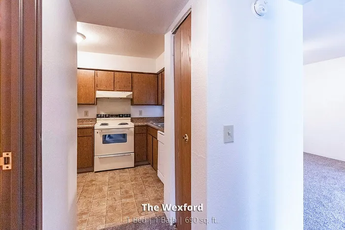 Cozy kitchen space with stylish wooden cabinets, sleek countertops, and a classic white stove in The Wexford apartment, 1 bed, 1 bath, 690 sq. ft.