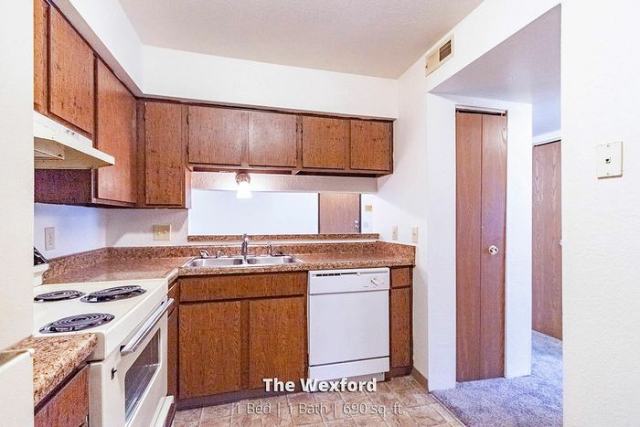 Charming kitchen in The Wexford featuring rich wooden cabinets, modern appliances, and a cozy design in a 1 bed, 1 bath apartment spanning 690 sq. ft.