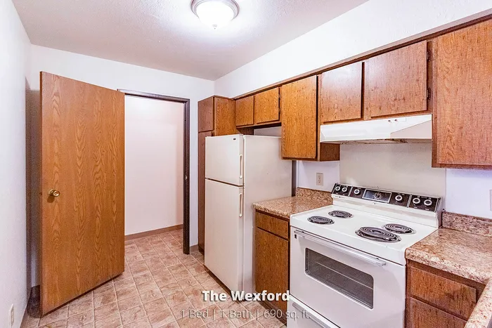 Charming kitchen in The Wexford featuring warm wood cabinetry, modern appliances, and ample counter space in a cozy 1 bed, 1 bath apartment.