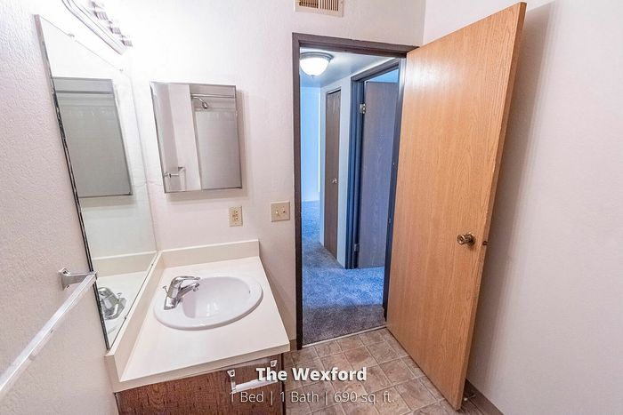 The Wexford apartment featuring a cozy bathroom with modern fixtures, leading into a welcoming hallway. 1 bed, 1 bath, 690 sq ft of comfortable living space.