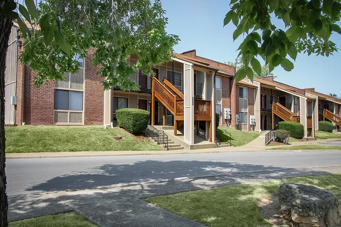 Charming apartment complex with rustic wooden staircases, lush manicured lawns, and inviting brick façades.
