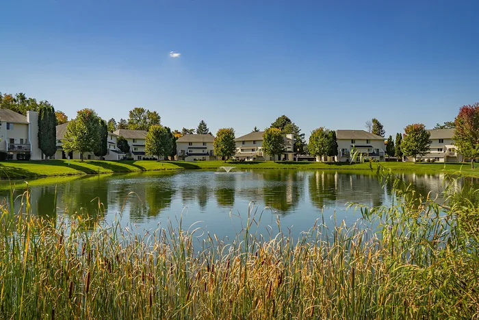 Charming apartment complex nestled by a serene pond with lush green landscaping and picturesque views.