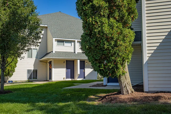 Charming townhouse with a modern exterior, set against a lush green lawn and shaded by mature trees.