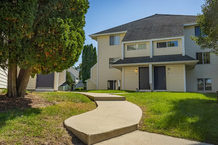 Charming apartment exterior with a welcoming curved walkway, nestled amongst lush green surroundings.