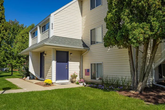 Charming townhouse exterior with blue doors, lush green lawn, and vibrant flowerbeds, nestled in a serene neighborhood.