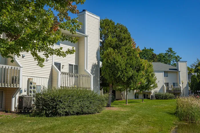 Charming townhouse exteriors with white siding, scenic green lawns, and lush landscaping under a clear blue sky.