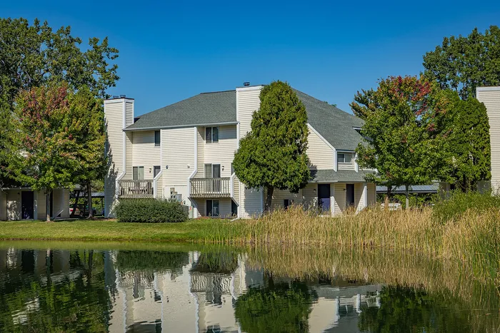 Charming lakeside apartment complex with modern architecture, surrounded by lush greenery and reflections in a serene pond.