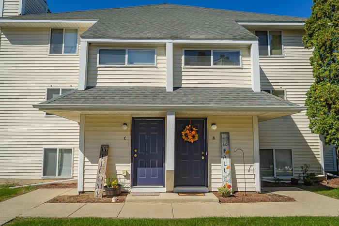 Charming duplex facade with two inviting blue doors, adorned with seasonal decorations and welcoming signs, under a bright blue sky.