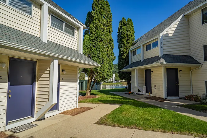 Charming townhouse entrance with modern blue doors, surrounded by lush greenery and a scenic water view.