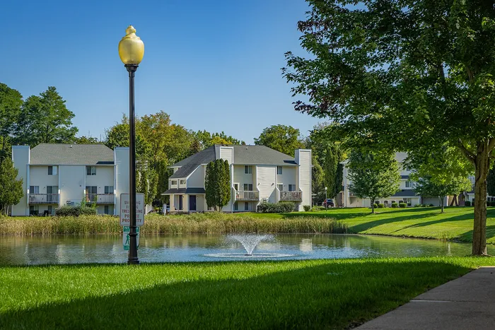 Charming lakeside apartments with lush greenery, tranquil pond, and inviting architecture under a clear blue sky.