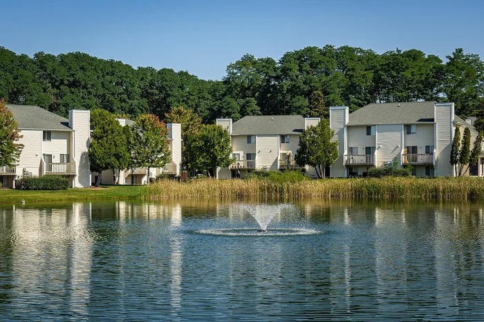 Charming lakeside apartments with fountains and serene wooded backdrop, perfect for tranquil living.