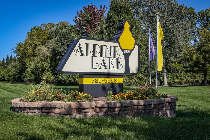 Charming Alpine Lake entrance sign set amidst lush greenery and vibrant flowers, inviting you to a serene community.