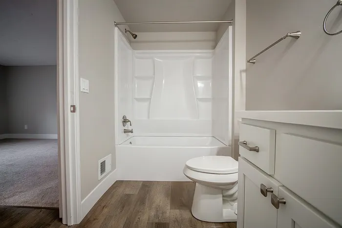 Modern bathroom featuring elegant white fixtures, a sleek bathtub with shelving, and stylish wood flooring.
