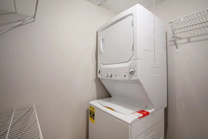 Bright laundry area featuring a space-saving stackable washer and dryer set, complemented by convenient shelving.