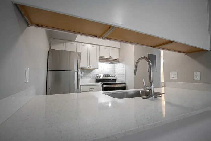 Modern kitchen with sleek stainless steel appliances, white cabinetry, and a polished quartz countertop featuring an elegant faucet.