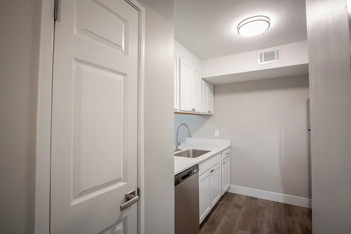 Sleek modern kitchen featuring elegant white cabinetry, stainless steel appliances, and laminate wood flooring.