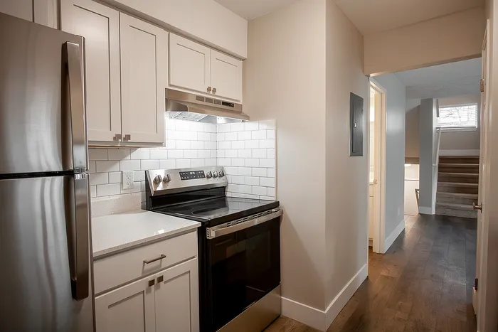 Modern kitchen with sleek stainless steel appliances, elegant white cabinetry, and bright subway tile backsplash, leading to a chic staircase.