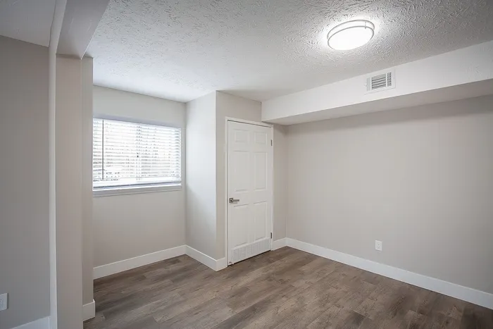 Bright, modern room with sleek wood flooring, ample natural light from the window, and fresh white walls, creating a peaceful living space.