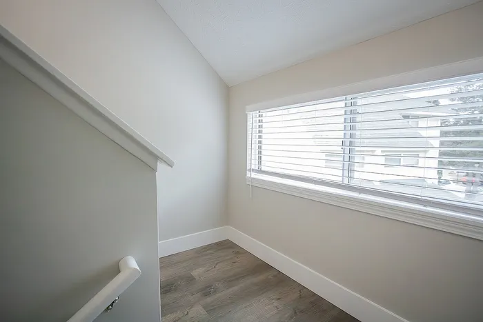 Bright stairway landing featuring large window with blinds, modern grey flooring, and sleek neutral walls.