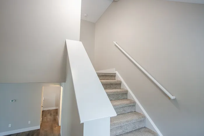 Inviting staircase with modern design leading to a spacious and bright upper level, featuring sleek carpeting and stylish railings.
