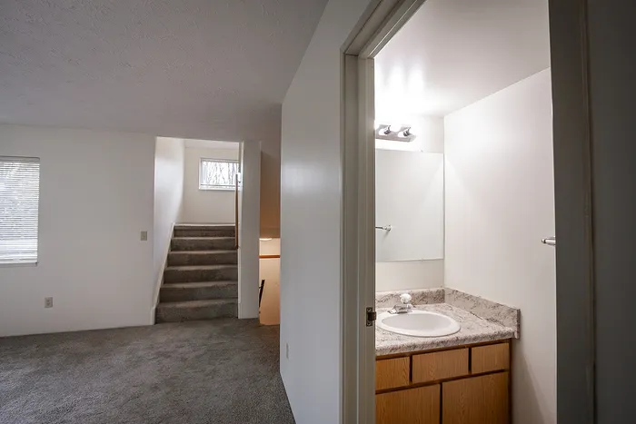 Inviting split-level apartment with plush carpeting, a bright bathroom, and an elegant staircase leading to upper floors.