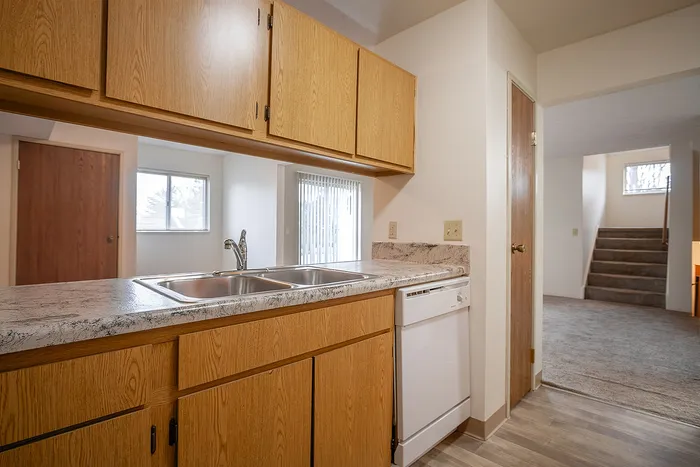 Bright and inviting kitchen with modern countertop, sleek faucet, and ample wooden cabinetry, leading to a cozy carpeted stairway.