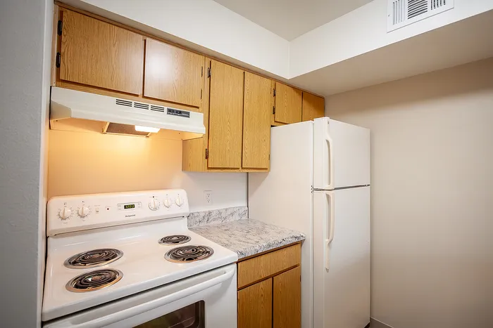 Bright kitchen with classic oak cabinets, white appliances, and marble-patterned countertops in a cozy apartment.