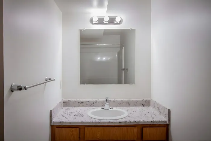 Modern bathroom with sleek marble countertop, stylish light fixture, and spacious mirror, exuding elegance and functionality.