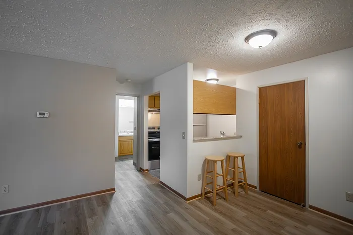 Cozy apartment interior boasting a modern kitchen with wooden cabinetry, stylish barstools, and sleek flooring.