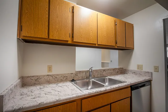 Charming kitchen with sleek marble-like countertops, wooden cabinets, and a modern stainless steel sink.