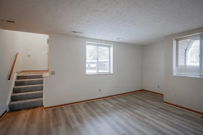 Inviting room with abundant natural light, featuring elegant flooring and a cozy staircase leading to upper levels.