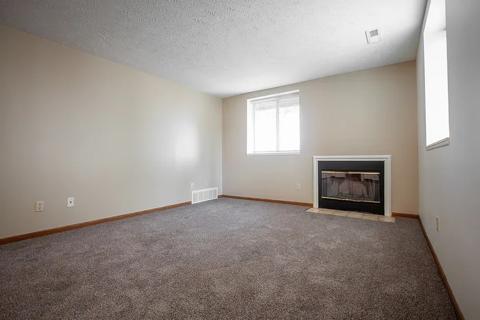 Inviting living room with plush carpeting, soft neutral walls, and a large window letting in natural light, featuring a charming fireplace for cozy evenings.