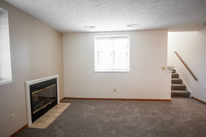 Inviting living space with plush carpet, cozy fireplace, and abundant natural light near a staircase.