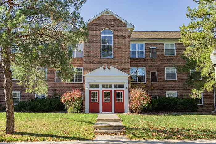 Charming brick apartment building with vibrant red doors, nestled in a lush green landscape, showcasing classic architectural elegance.