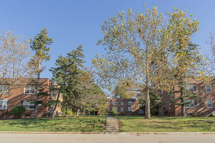 Charming brick apartment buildings surrounded by lush greenery and tall trees under a clear blue sky.