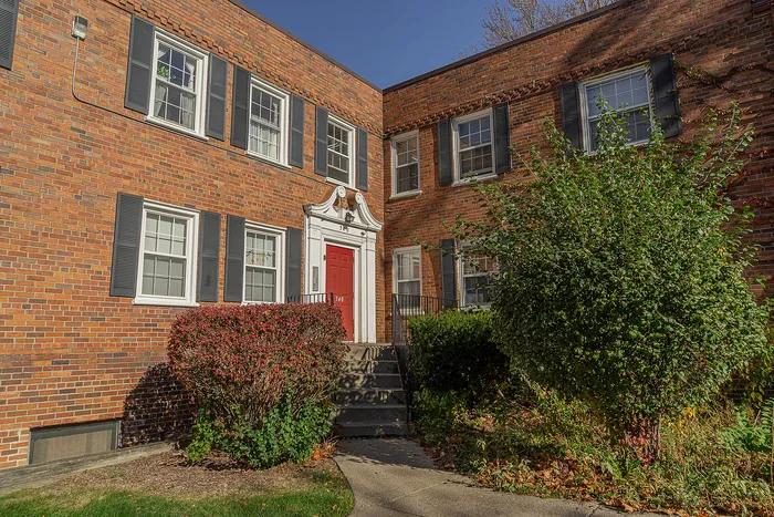 Charming brick apartment building with classic red door and lush greenery, offering a welcoming environment.