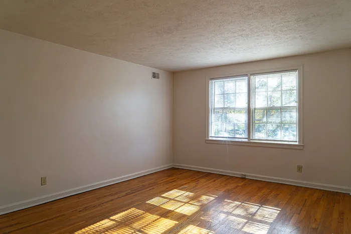 Bright, sunlit room with polished hardwood floors and a large window, perfect for a cozy living space.